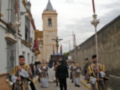Una procesión religiosa en un pueblo, con personas vestidas de trajes tradicionales y una iglesia en el fondo.