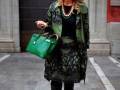 Una mujer con una chaqueta de camuflaje y un vestido verde, sosteniendo una bolsa verde.