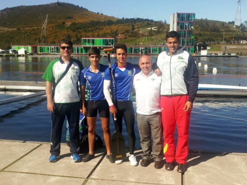 Equipo de remo posando junto al lago con un instructor en un día soleado.