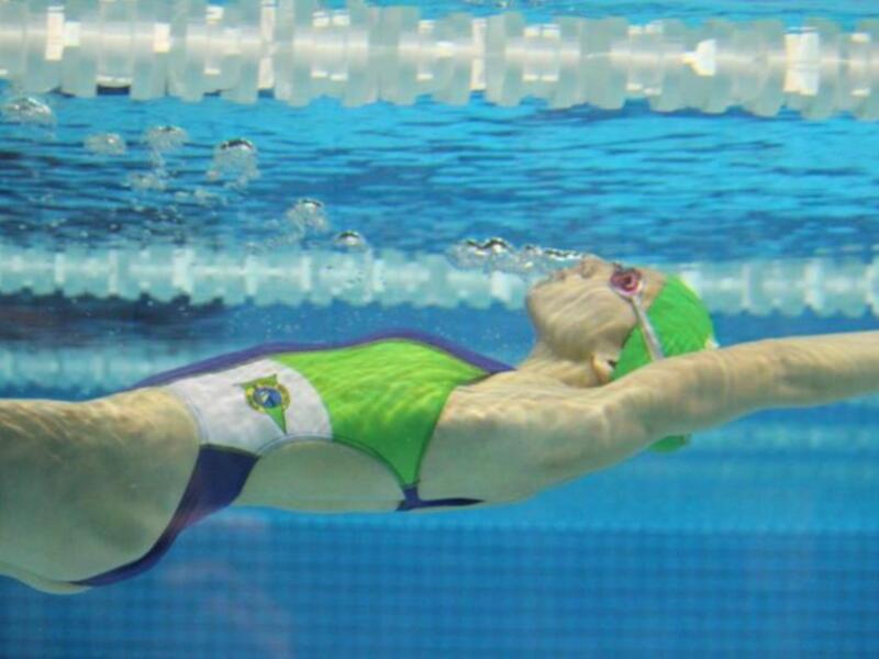 Una nadadora en traje de baño verde y blanco, realizando el estilo de nado braza en una piscina olímpica.