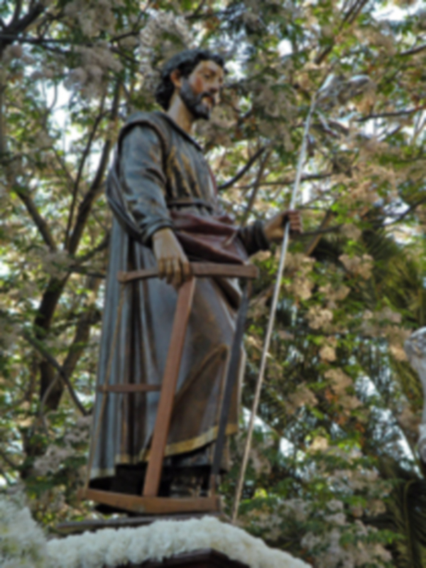 Estatua de San José sosteniendo un bastón y una caja, rodeada de flores y árboles en flor.