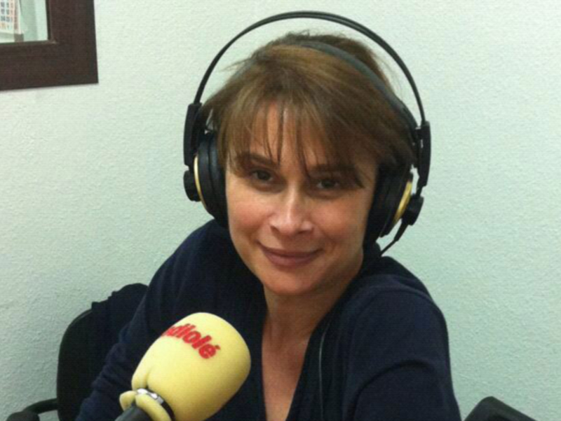 Una mujer con auriculares y micrófono en una radio, sonriendo.