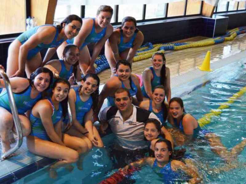 Equipo de natación y entrenador posando juntos en la piscina.