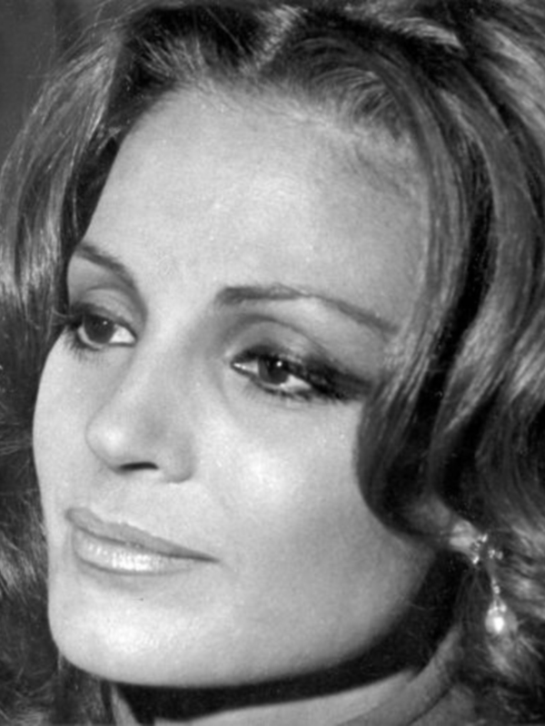 Retrato en blanco y negro de una mujer con cabello largo y rizado, maquillaje clásico y pendientes de perla.