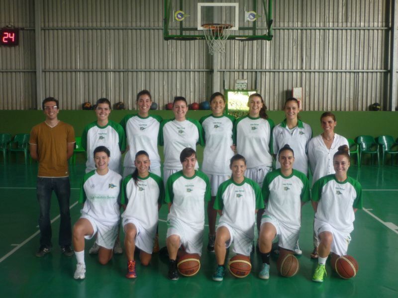 Equipo de baloncesto femenino en uniforme blanco y verde, posando en una cancha deportiva.