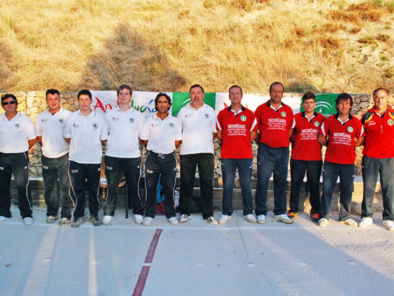 Equipo deportivo posando en una pista de bádminton con un cartel de 'Andalucía' en el fondo.