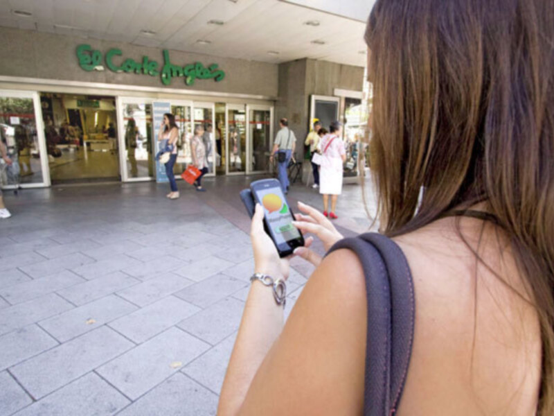 Persona usando un teléfono móvil frente a la entrada de El Corte Inglés.