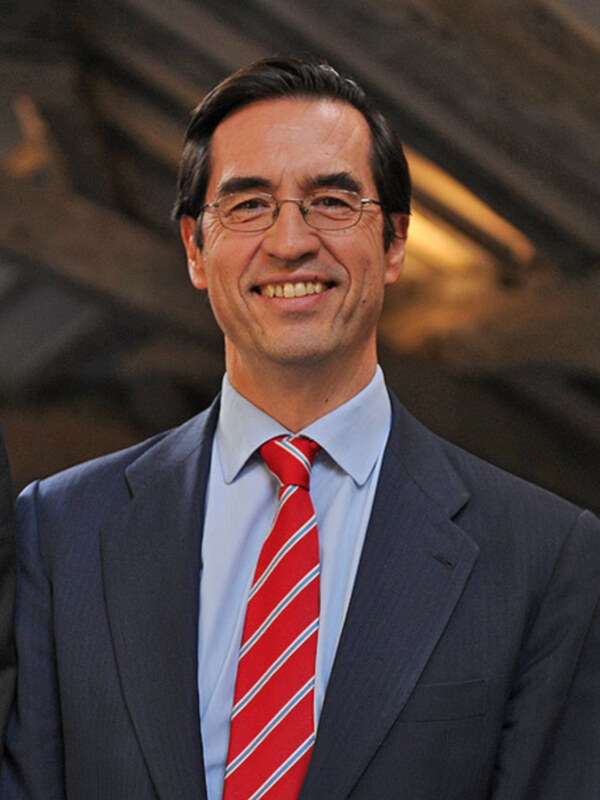 Hombre sonriente en traje y corbata roja, fondo borroso