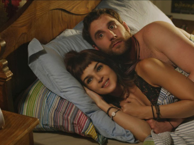 Un hombre y una mujer acostados juntos en una cama, sonrientes y relajados.