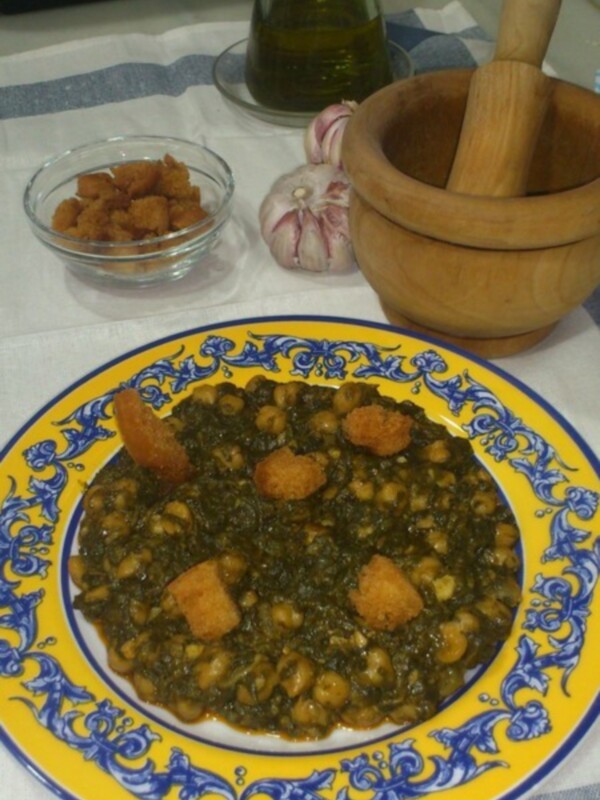 Plato de lentejas con espinacas y pan frito, acompañado de ajo y aceite de oliva.