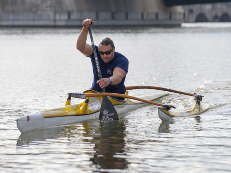Un hombre rema en un kayak en un río bajo un puente.