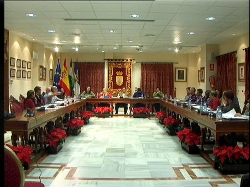 Reunión de trabajo en un salón formal con banderas y flores rojas en la mesa.