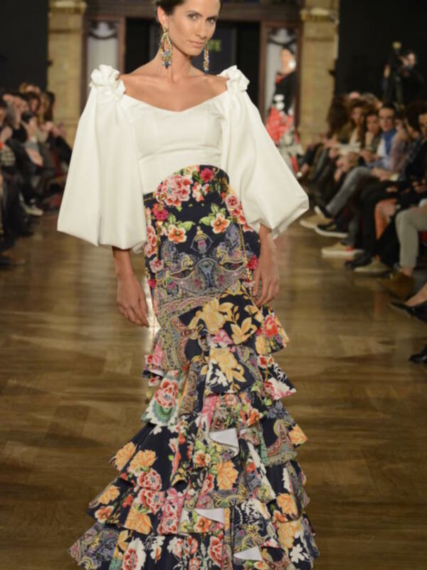 Modela en desfile de moda con vestido blanco y falda de flores coloridas, destacando la textura y el diseño floral.