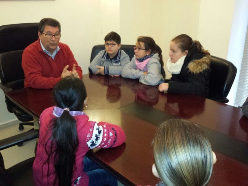 Un grupo de personas sentadas en una mesa de conferencia, con una persona en el extremo izquierdo y cuatro personas en el extremo derecho, todos mirando hacia la izquierda.