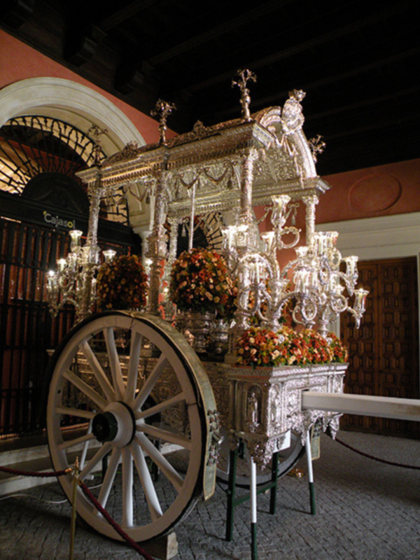 Elegant silver carriage adorned with flowers and chandeliers, displayed indoors.