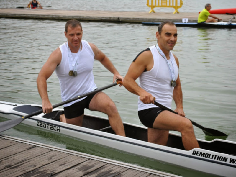 Dos atletas con medallas posan en un bote de remo en un entorno acuático.