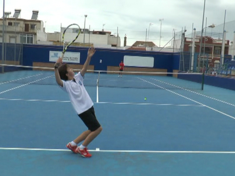 Joven jugador de tenis en acción durante un entrenamiento en una cancha de césped artificial.