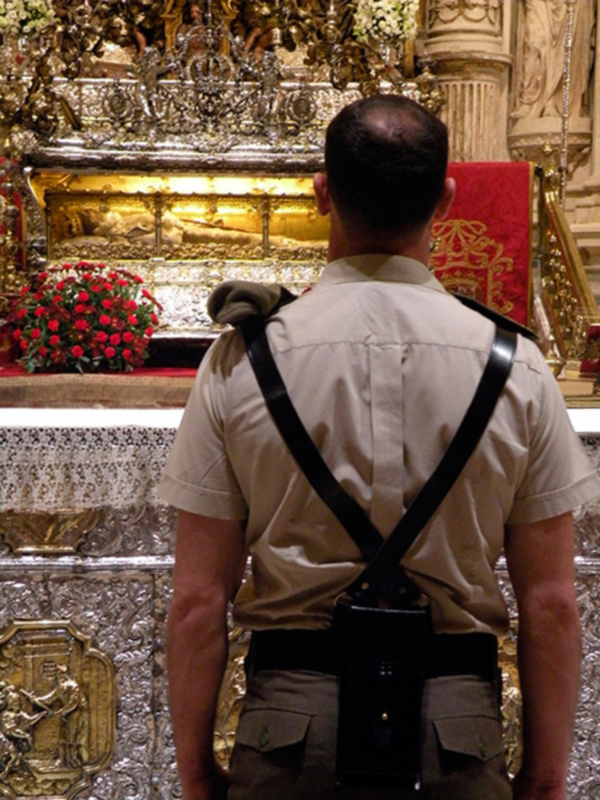 Persona de espaldas observando una reliquia en un altar ornado, rodeado de detalles dorados y flores rojas.