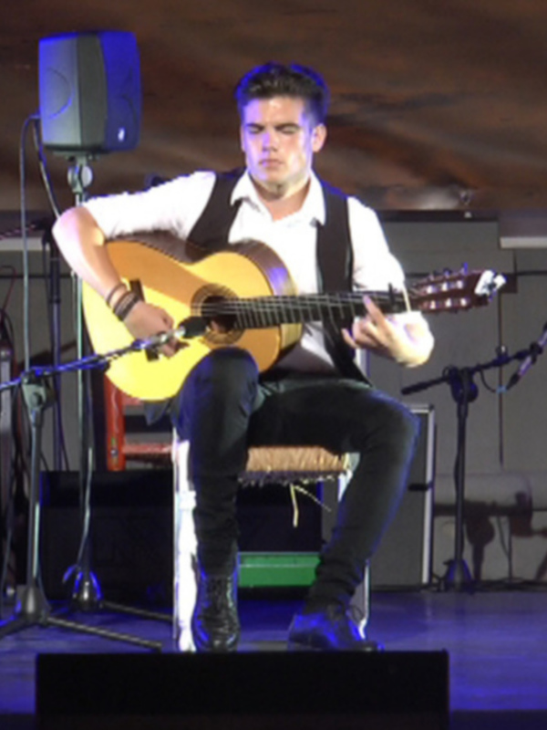 Músico tocando la guitarra acústica en un escenario con sillas decorativas y altavoces.