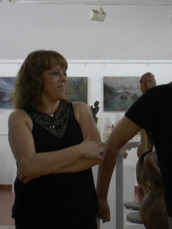 Personas dialogando en una galería de arte con obras expuestas en el fondo.
