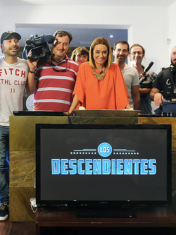 Una escena de un programa de televisión con una presentadora en el centro, rodeada por varios camarógrafos y un monitor en el frente mostrando el logo del programa 'Los Descendientes'.