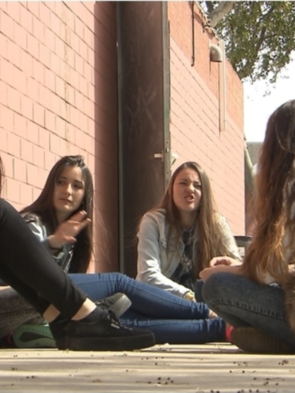 Un grupo de jóvenes se reúne en un patio, sentados en el suelo y conversando.
