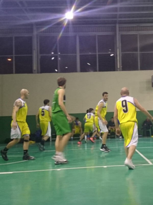Jugadores de baloncesto en acción durante un partido en una cancha interior iluminada.