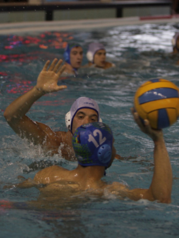 Juego de voleibol de agua en una piscina con jugadores usando cascos y pelotas.
