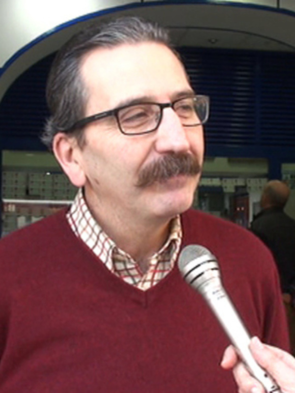 Hombre con bigote y gafas hablando en un microfono en una tienda.