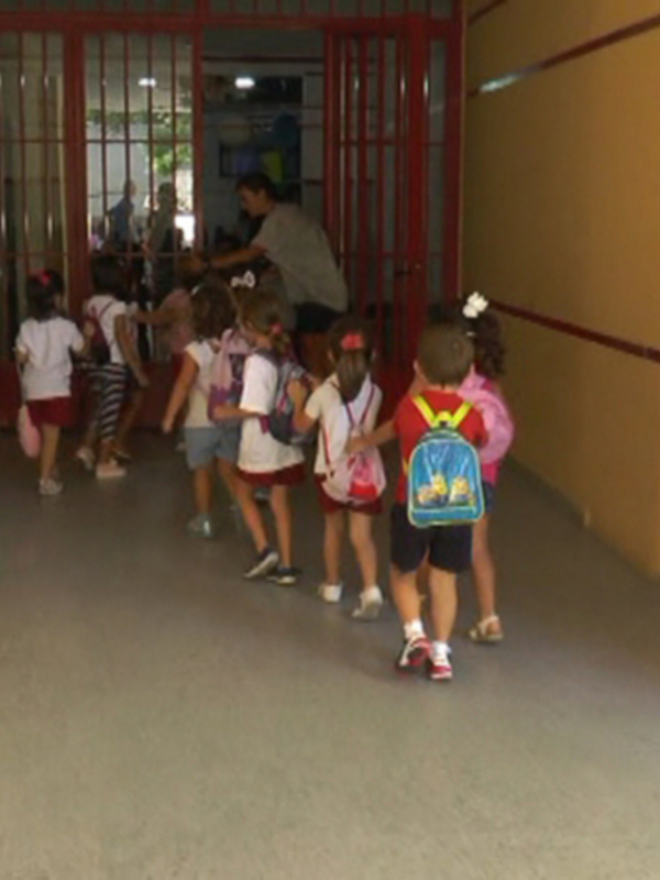 Niños caminando en un pasillo de una escuela, con mochilas y uniformes coloridos.