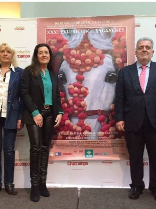 Grupo de personas posando frente a una cartel informativo sobre la XXXI Exposición de Enganches en Sevilla, con una imagen de un caballo en el fondo.