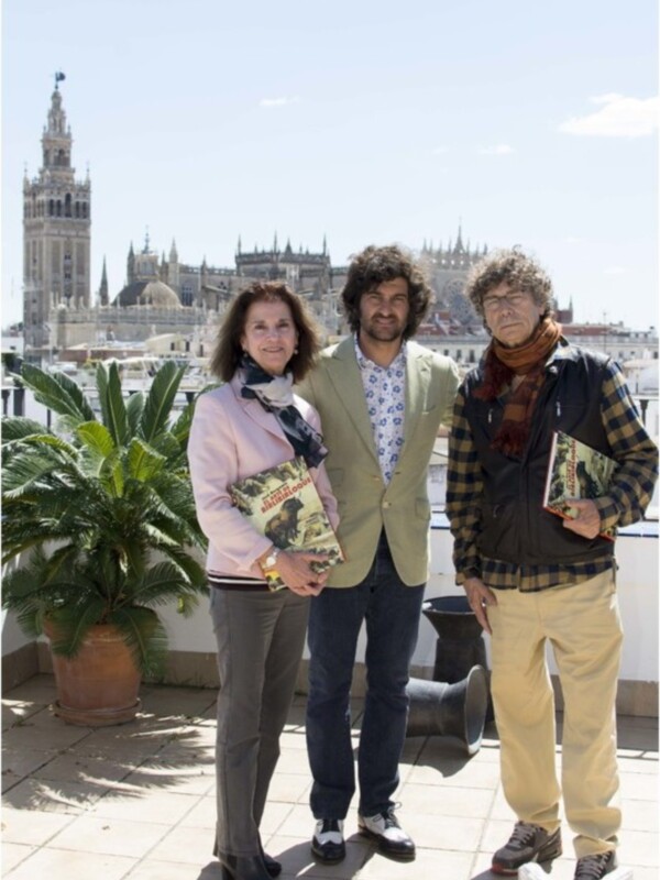 Tres personas posan con libros frente a la Catedral de Sevilla y la Giralda.