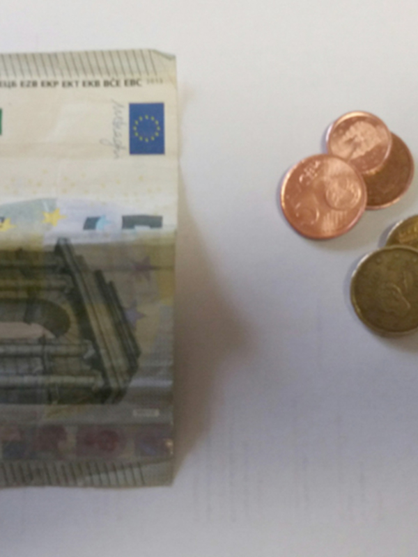 Un billete de 5 euros y varias monedas de diferentes denominaciones sobre un fondo blanco.