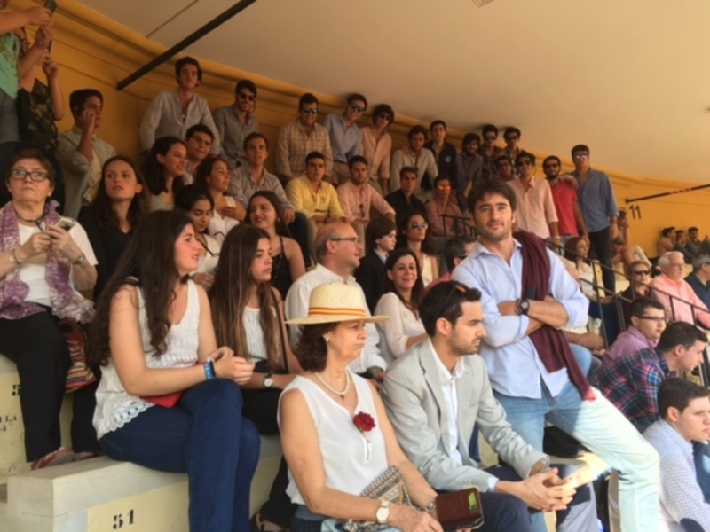 Un grupo de personas sentadas en gradas, algunas con sombreros y otros con relojes, en un evento público.