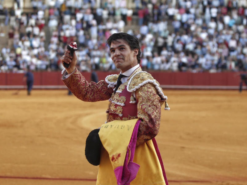 Un torero celebra en el ruedo tras una actuación exitosa, rodeado por un público entusiasmado.