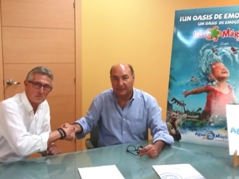 Dos hombres se saludan en una reunión de negocios frente a un cartel promocional de 'Isla Mágica'.