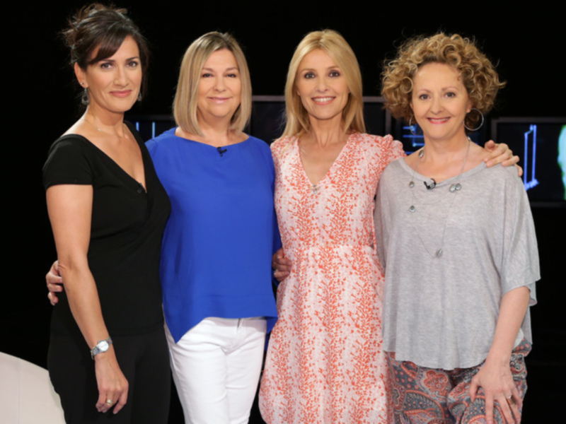 Cuatro mujeres sonríen y posan juntas en un estudio de televisión.