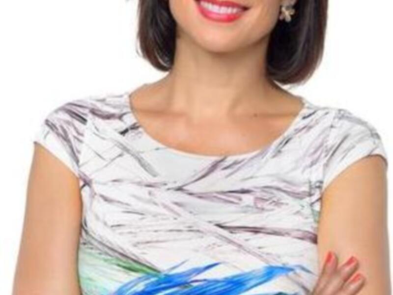 Retrato de una mujer sonriente con brazos cruzados, vistiendo una blusa de estampado floral y un reloj rosa.