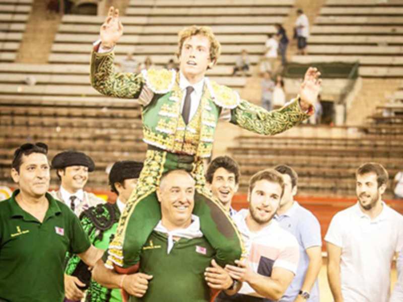 Un torero celebra triunfante en la plaza de toros, rodeado por sus seguidores y compañeros.