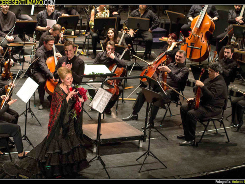Baile flamenco en escenario con orquesta de cuerdas en el fondo.