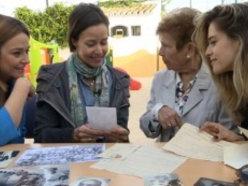 Cuatro mujeres revisan documentos históricos en un ambiente al aire libre, rodeadas de flores y artefactos.