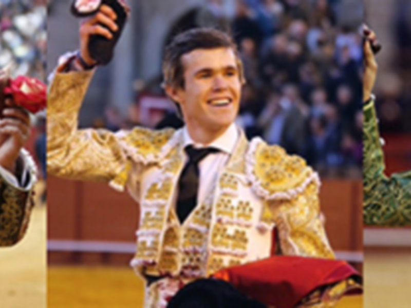 Tres toreros celebrando con la mano en alto en un ruedo de toros.