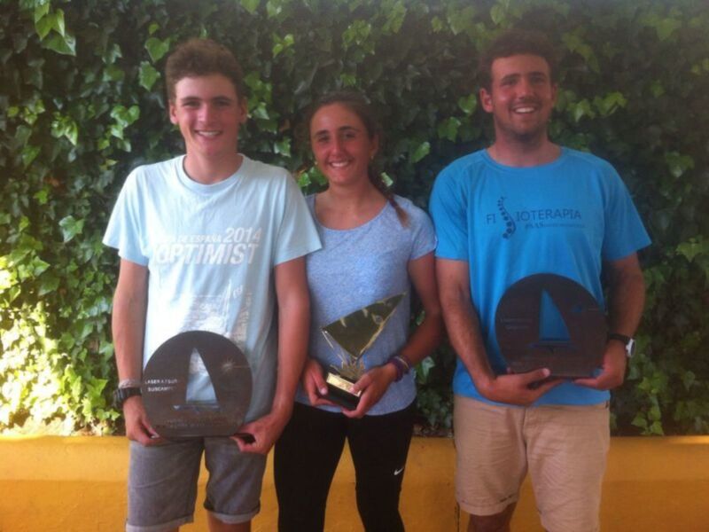 Tres jóvenes sonríen con trofeos en una ceremonia de premiación al aire libre.