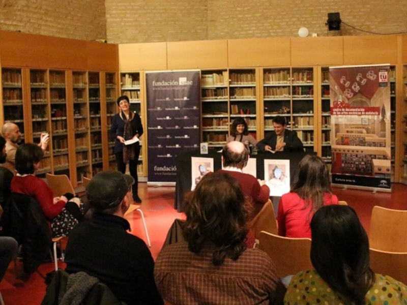 Lectura en biblioteca con audiencia atenta y carteles de la Fundación SAE.