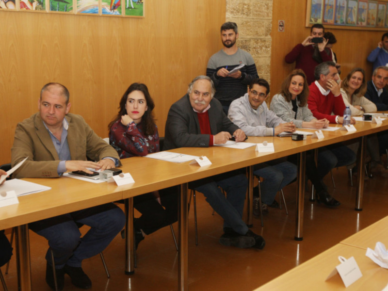 Una reunión formal con personas sentadas en una mesa, algunos escribiendo y otros observando.