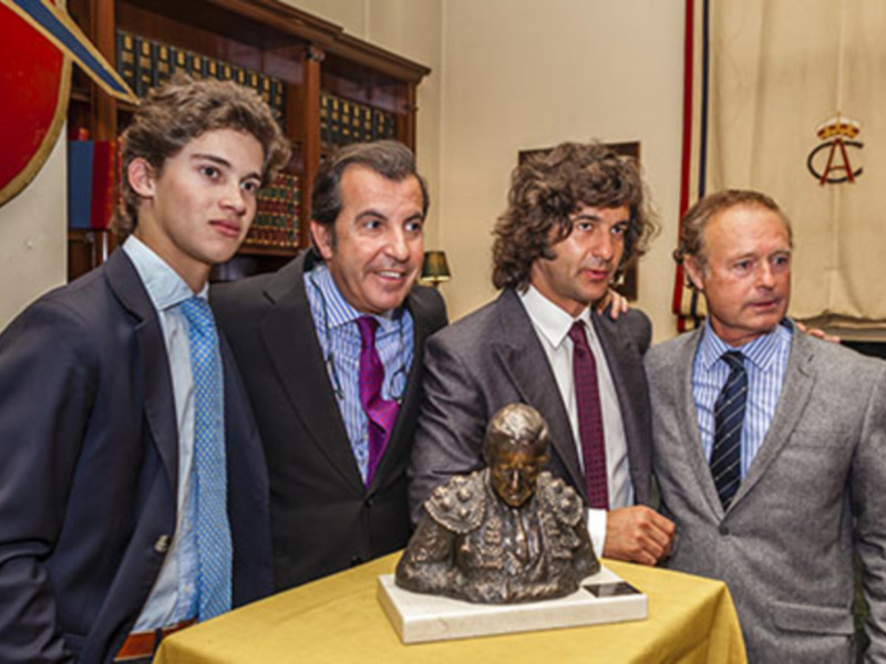 Ceremonia conmemorativa con una escultura de busto y cuatro personas en trajes de negocios.