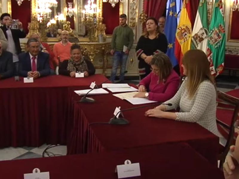 Una reunión formal en un entorno ceremonial, con personas sentadas en mesas rojas, banderas nacionales en el fondo y una persona escribiendo en un papel.