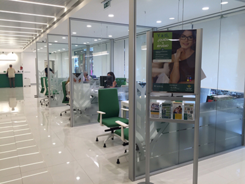 Interior de una oficina moderna con mesas verdes y un cartel informativo en la pared.