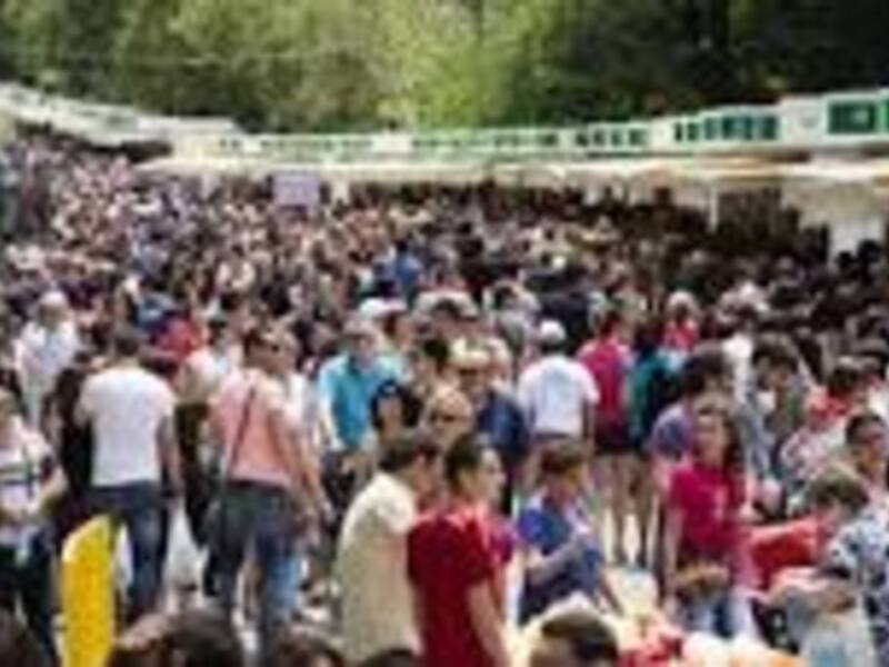 Gran concurrencia en un evento al aire libre, con personas caminando y disfrutando en un entorno verde.