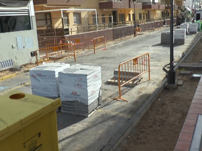 Zona de construcción con contenedores de basura y barreras de seguridad al lado de edificios residenciales.